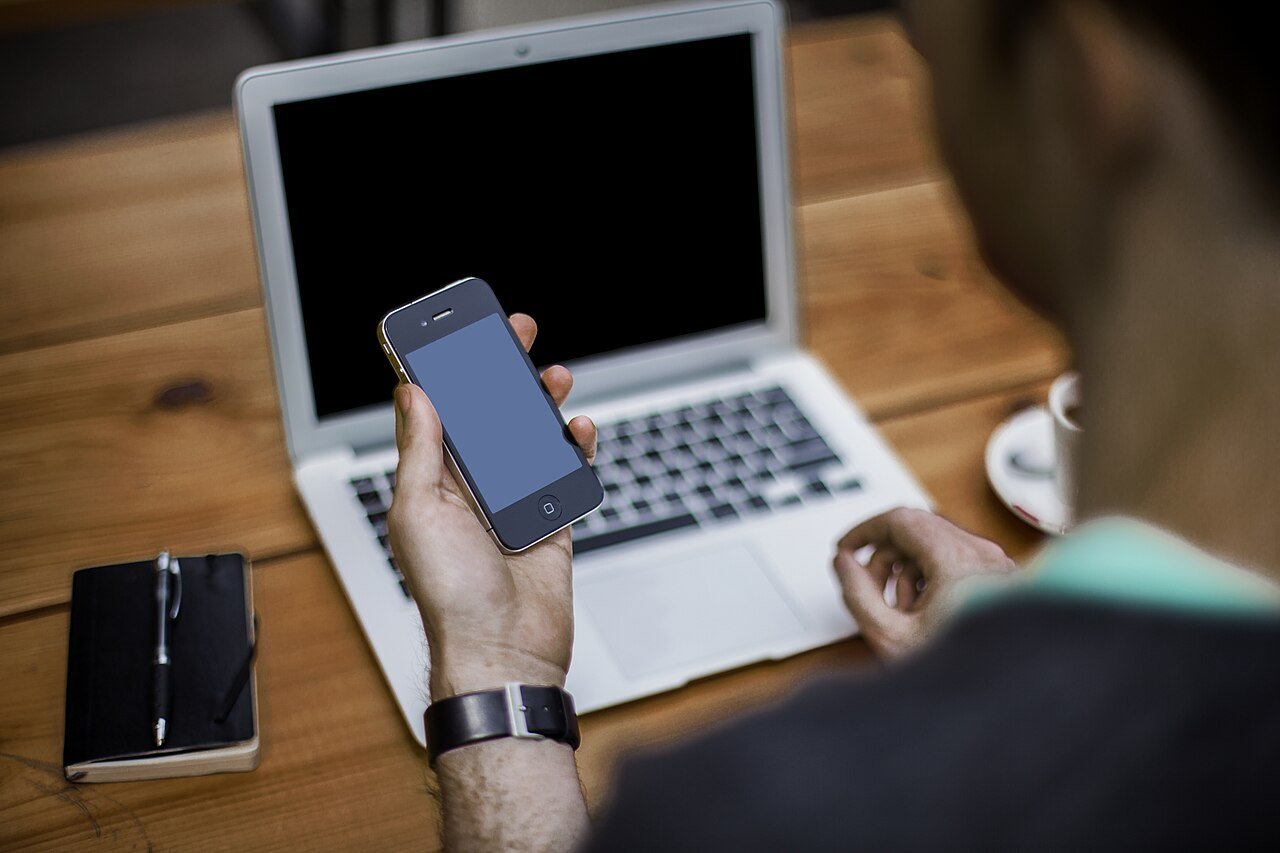 A hand holding a smartphone at a desk, checking a message